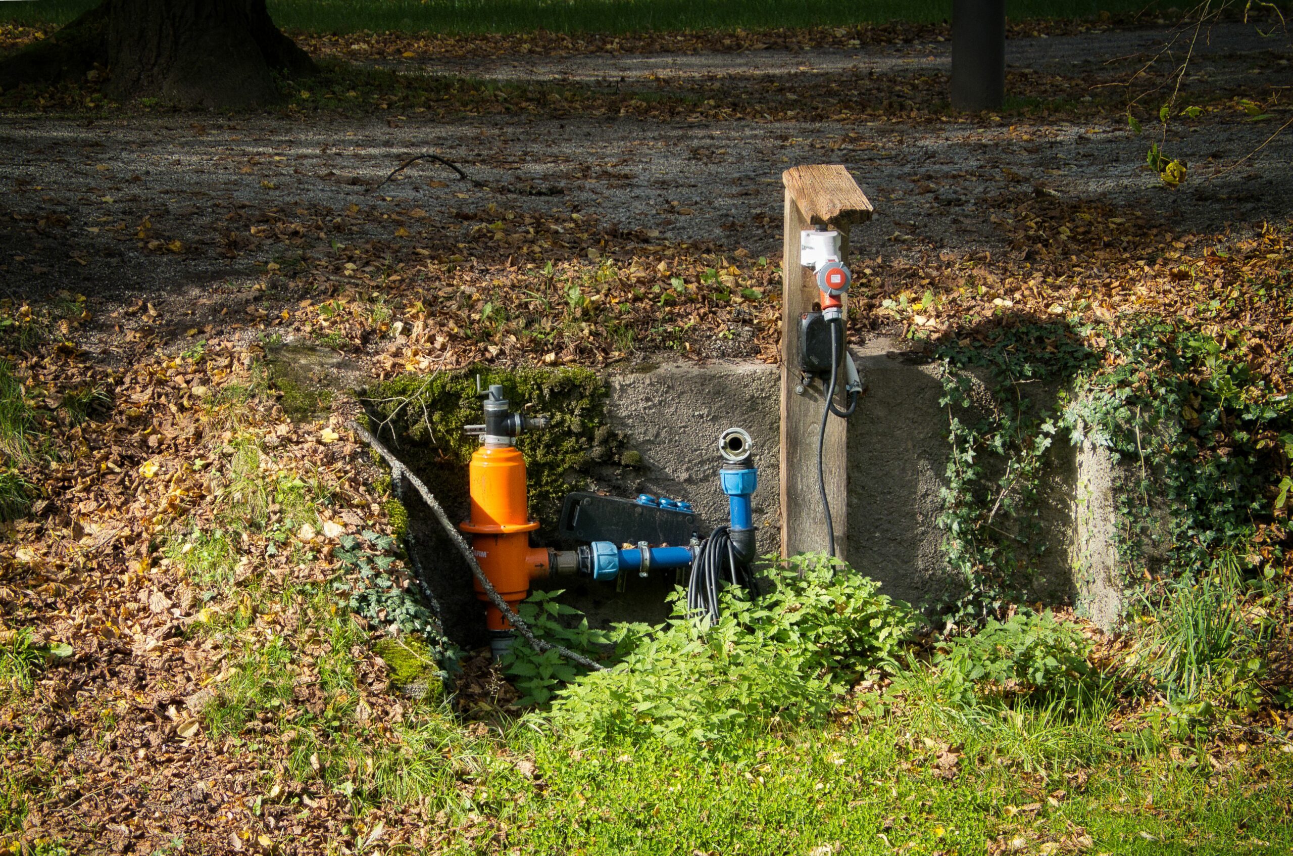 Water pipe system in a park with surrounding greenery and autumn leaves.
